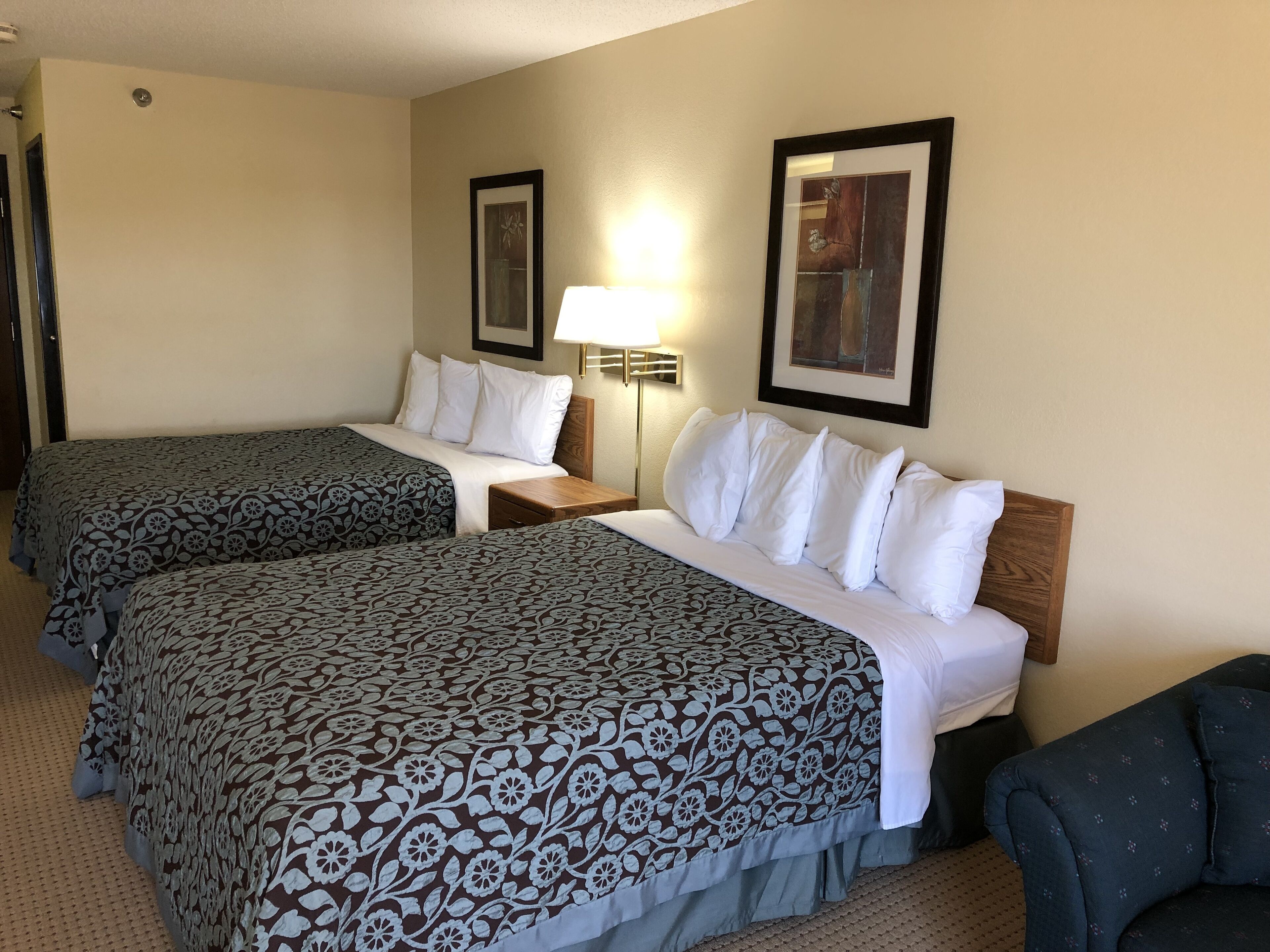 Een hotelkamer met twee bedden, een nachtkastje, een lamp en twee ingelijste foto’s aan de muur.