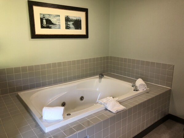 A bathroom with a large bathtub, grey tiles, and a framed picture above the tub.