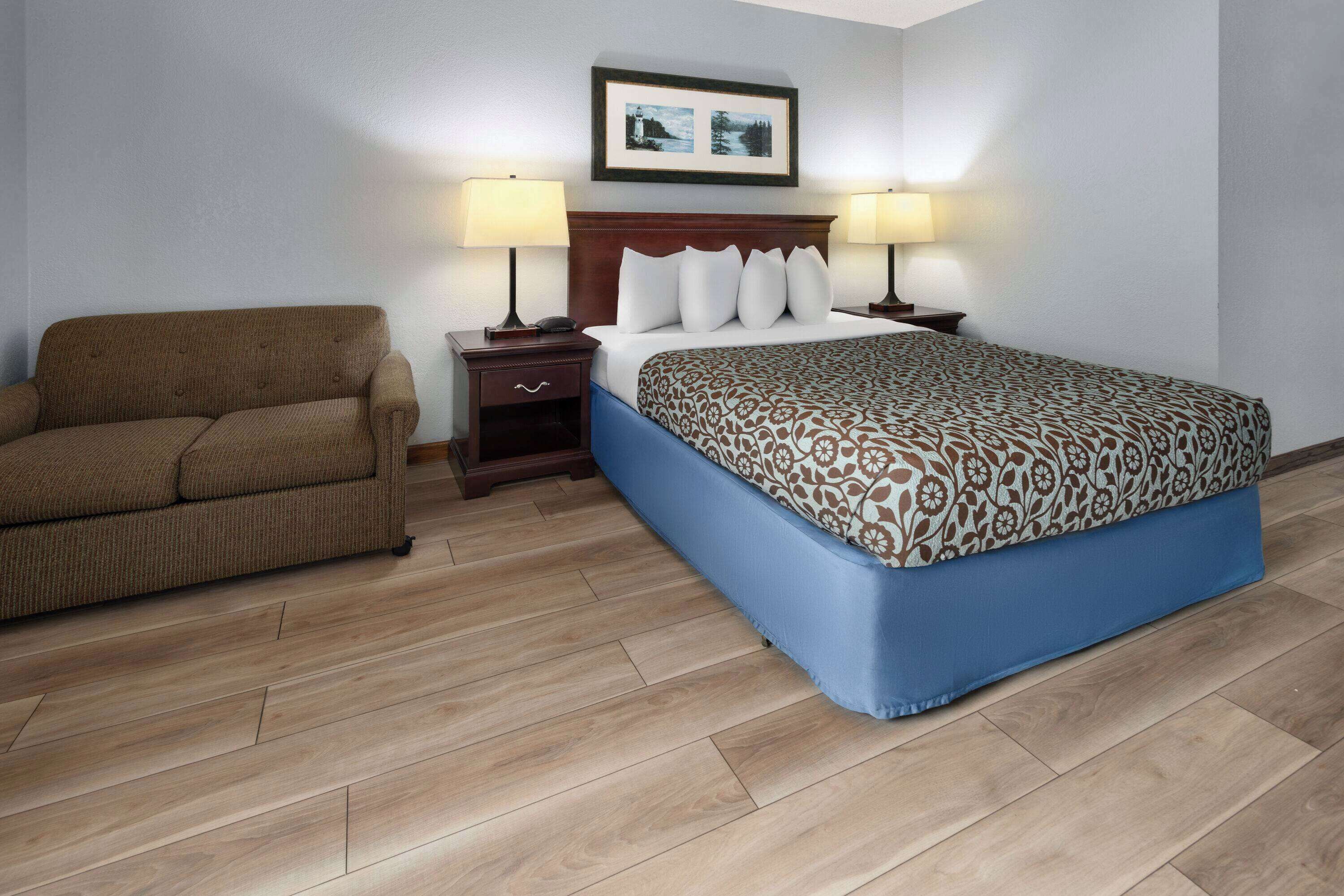 Habitación de hotel con cama, sofá, dos mesitas de noche con lámparas y un cuadro en la pared.