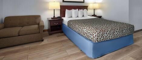 Habitación de hotel con cama, sofá, dos mesitas de noche con lámparas y un cuadro en la pared.