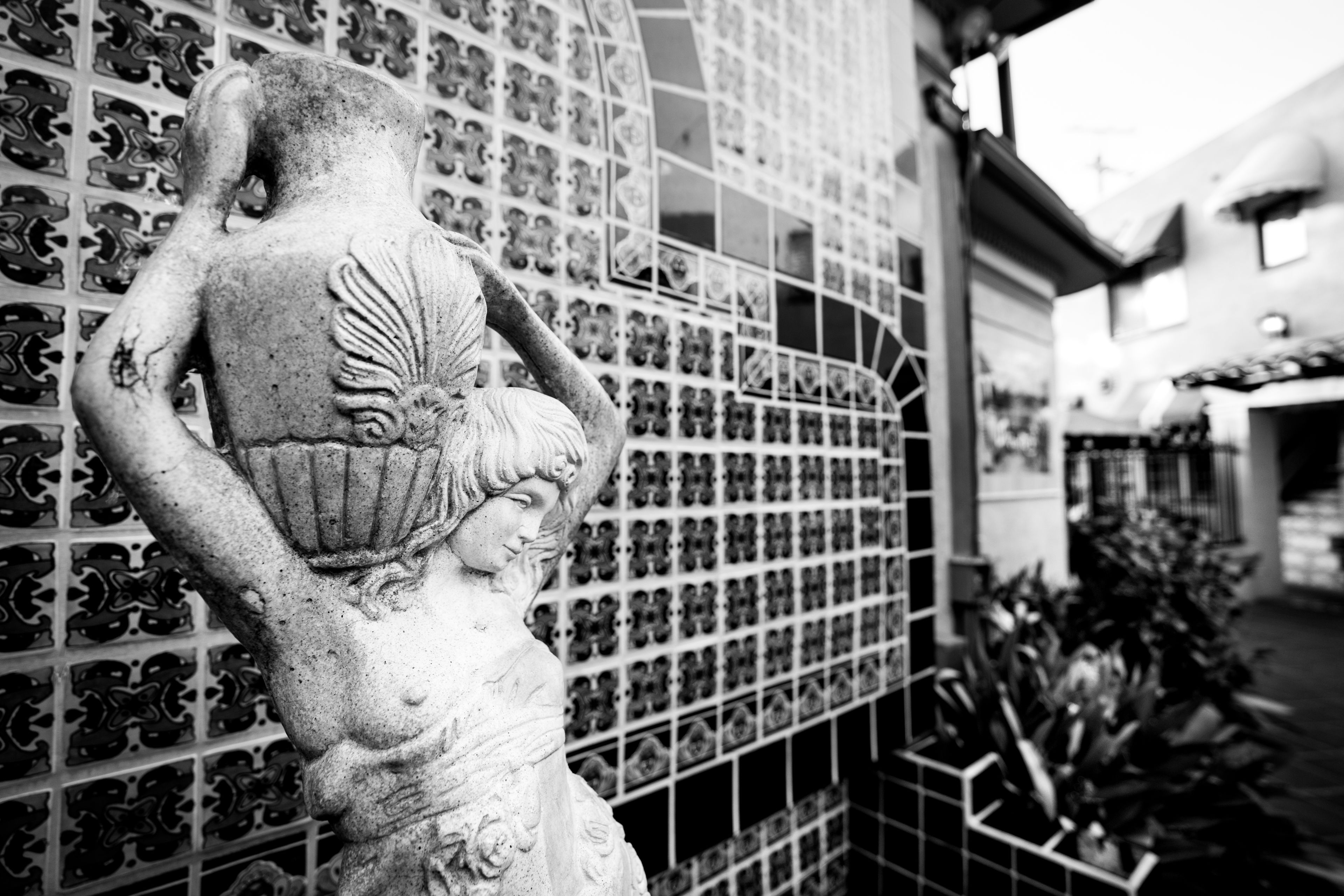 A statue of a woman with a child, positioned against a wall with a grid of patterned tiles.