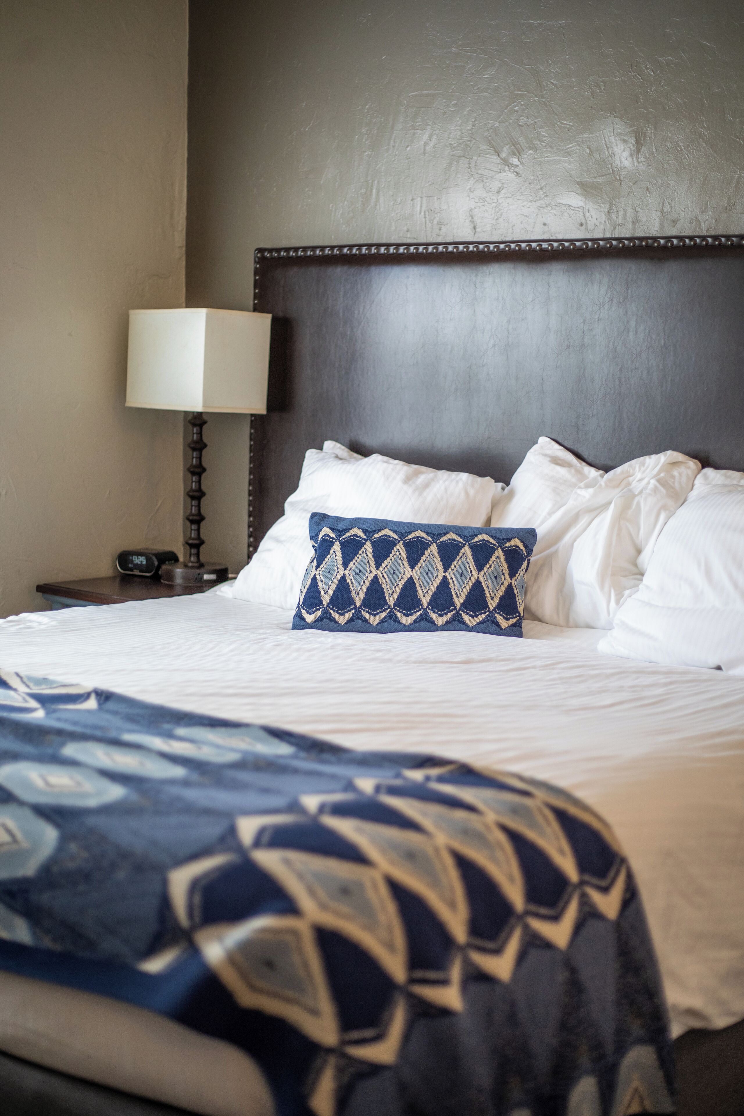A neatly made bed with white linens and a patterned throw blanket.