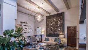 Ein großzügiger Wohnbereich mit einer großen Couch, zwei Sesseln, einem Couchtisch und Zimmerpflanzen. Es gibt ein dekoratives Wandbild und eine Chandelüster.
