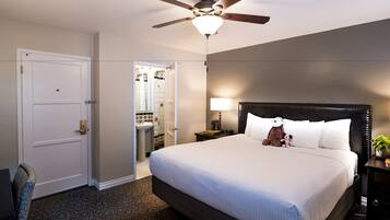 A hotel room with a large bed, a ceiling fan, a nightstand with a lamp, and a view of the bathroom.