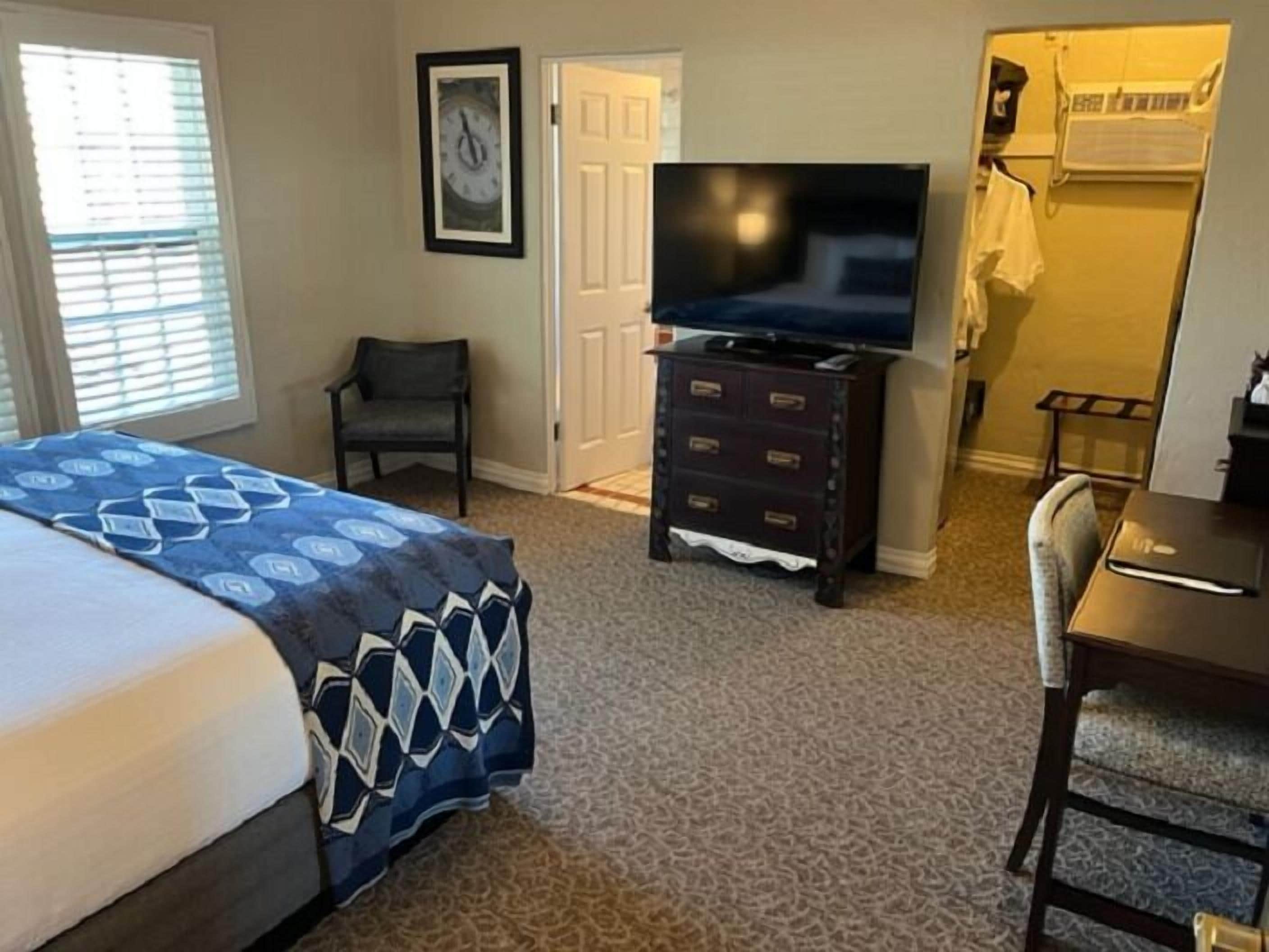 A hotel room with a bed, a dresser, a chair, a desk, a television, and a door.
