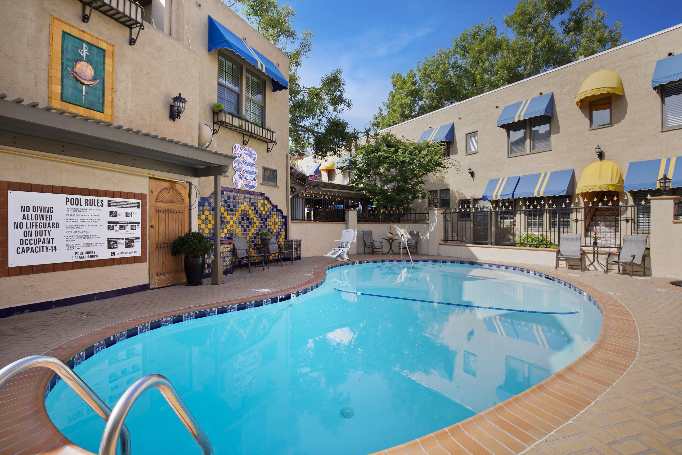 A swimming pool with a tiled edge, a signboard with pool rules, and a patio area with outdoor seating.
