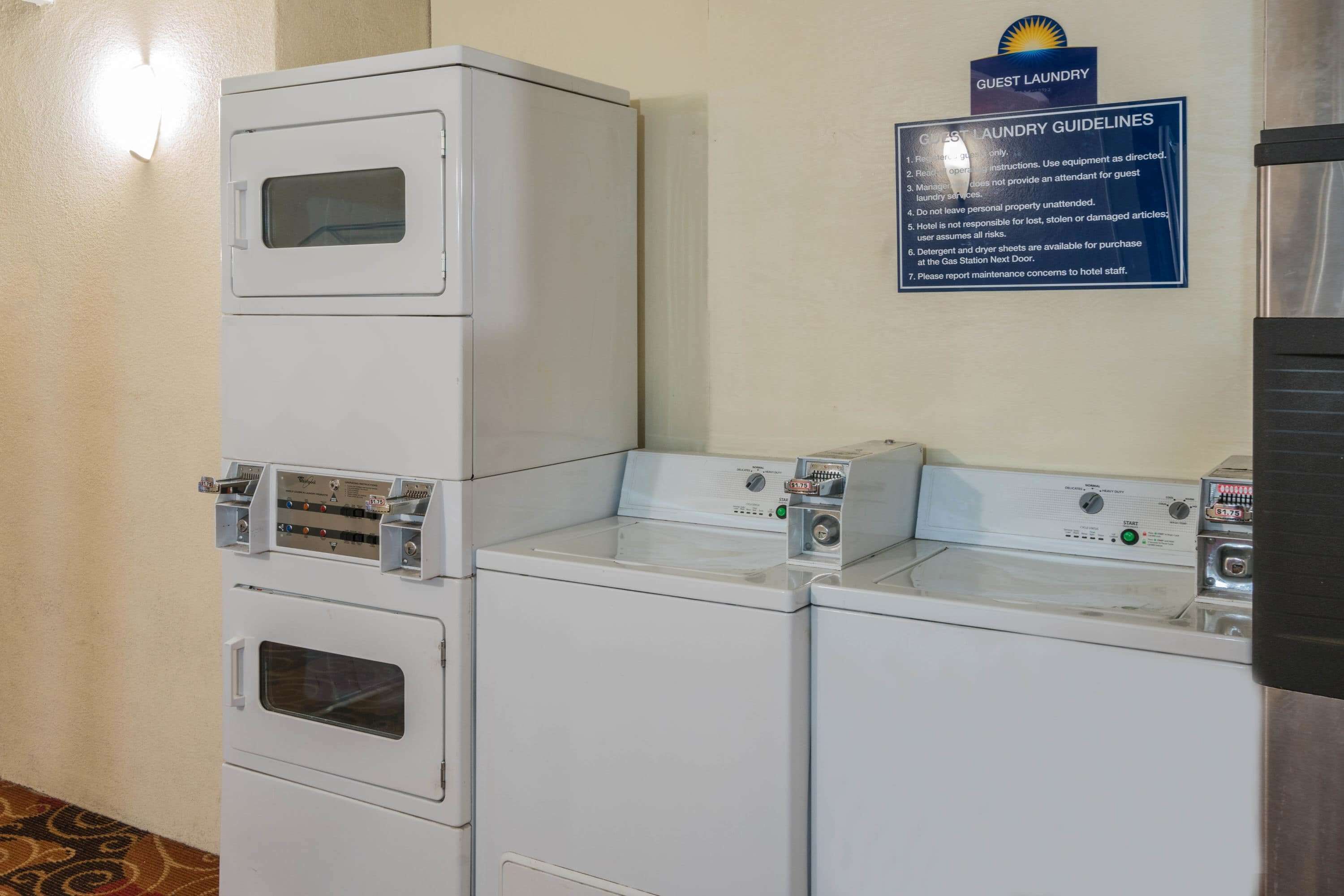 A laundry area with stacked washers and dryers, a sign with laundry guidelines, and a wall-mounted light.
