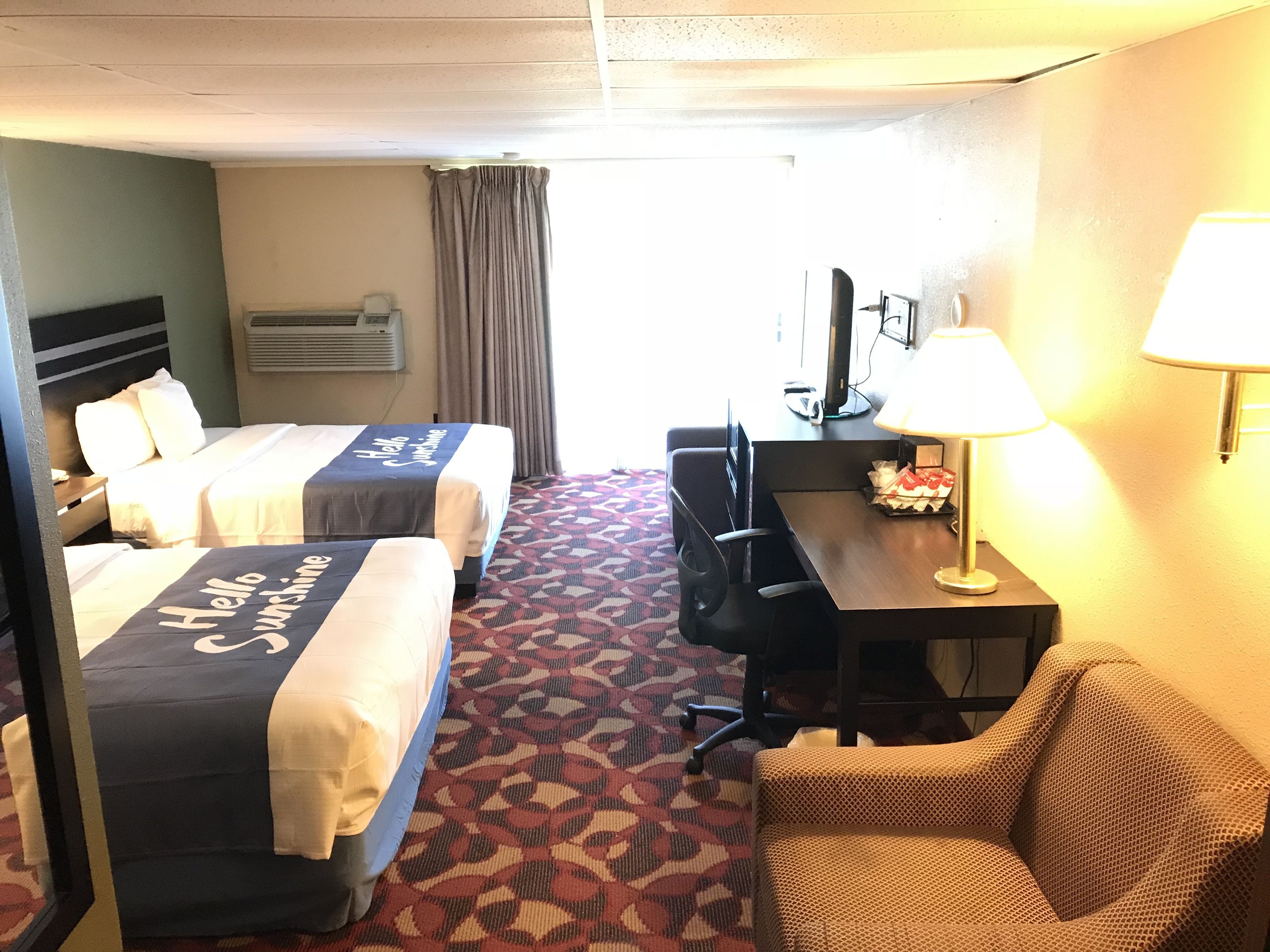 Habitación de hotel con dos camas, un escritorio, una silla y una lámpara.