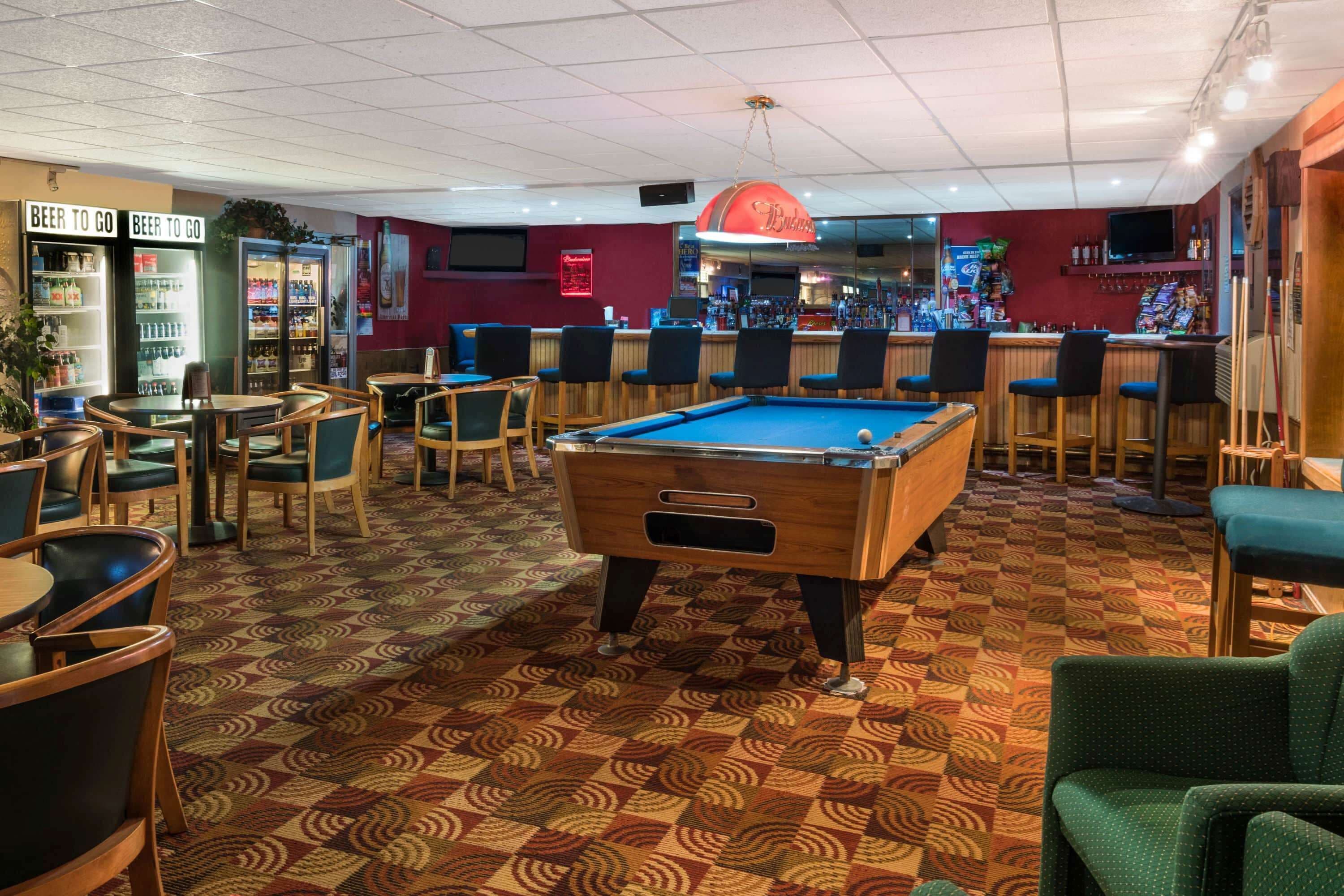 A pool table in a bar area with stools and a bar counter.