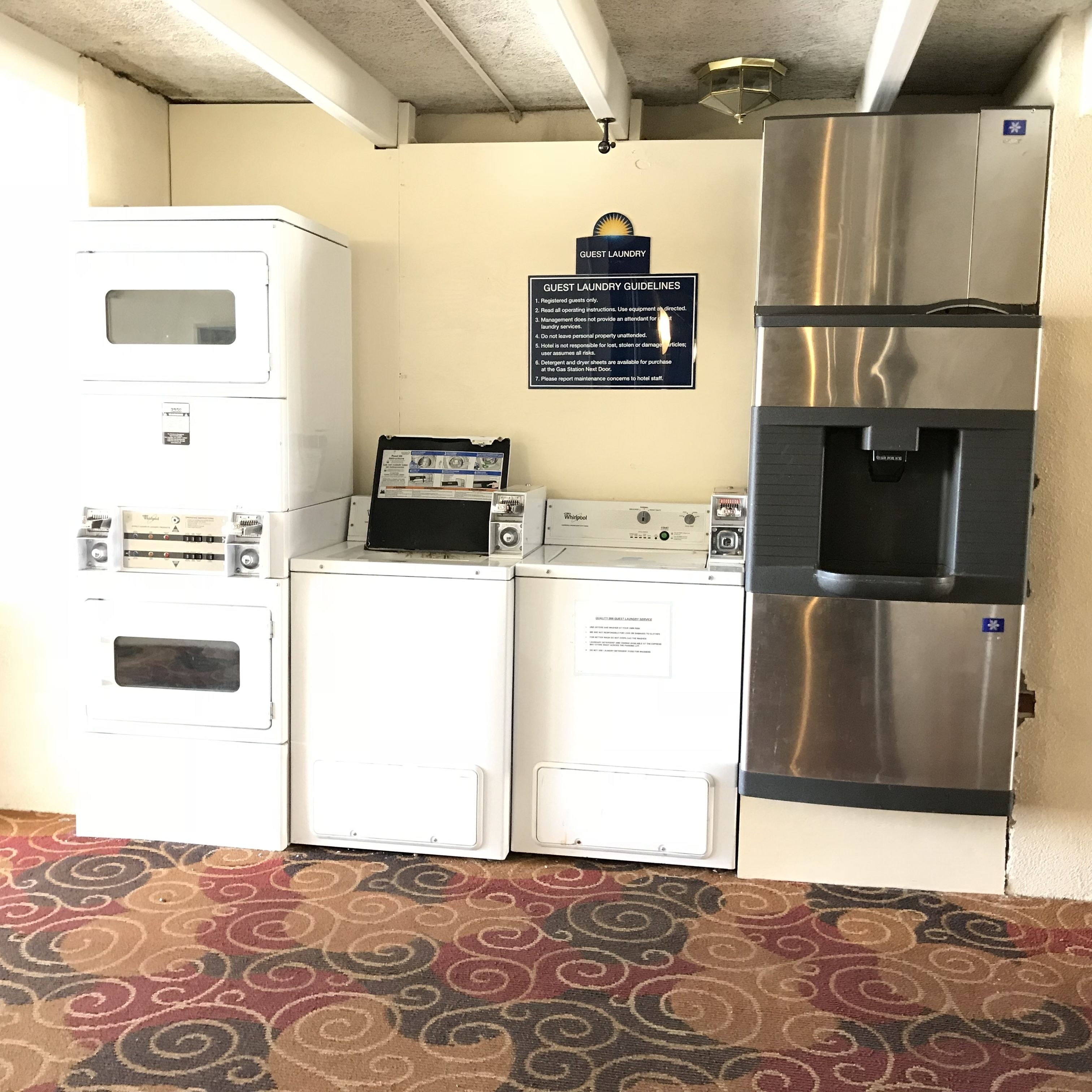 A laundry room with a Whirlpool washer, a dryer, and a refrigerator. There is a sign with guest laundry guidelines on the wall.