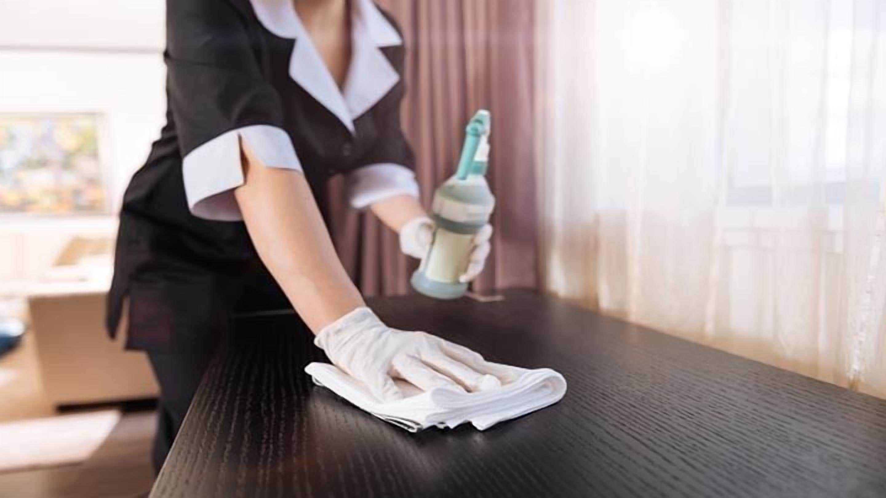 A person cleaning a dark wooden table with a cloth and a spray bottle.