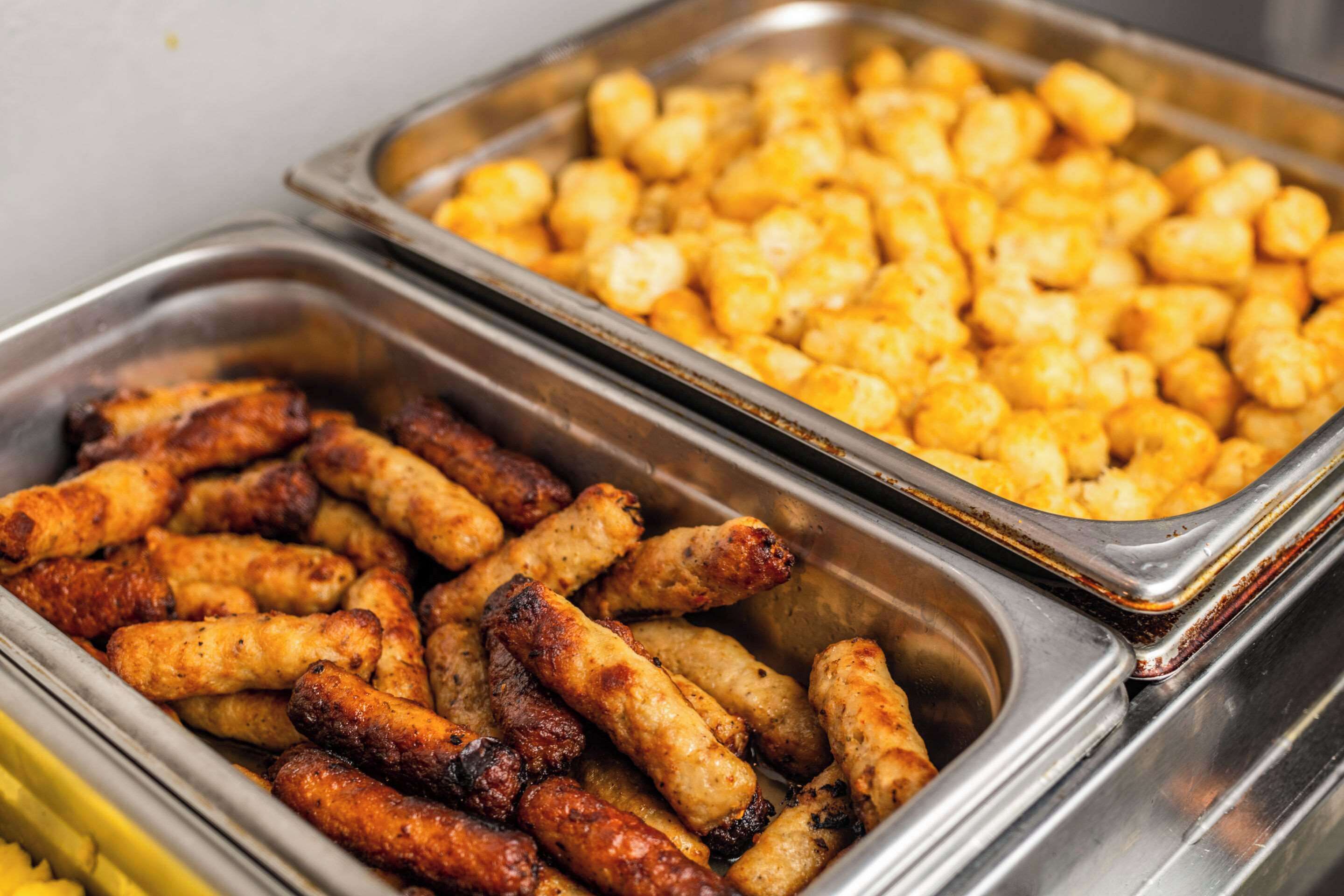 A buffet with trays of food including sausages and tater tots.