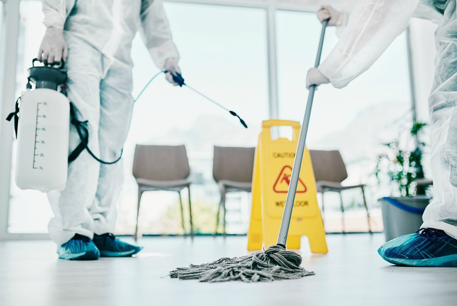 A person mopping the floor in a room with chairs and a caution sign.