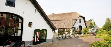A cobblestone courtyard with traditional white buildings, a black metal bench, and potted plants.