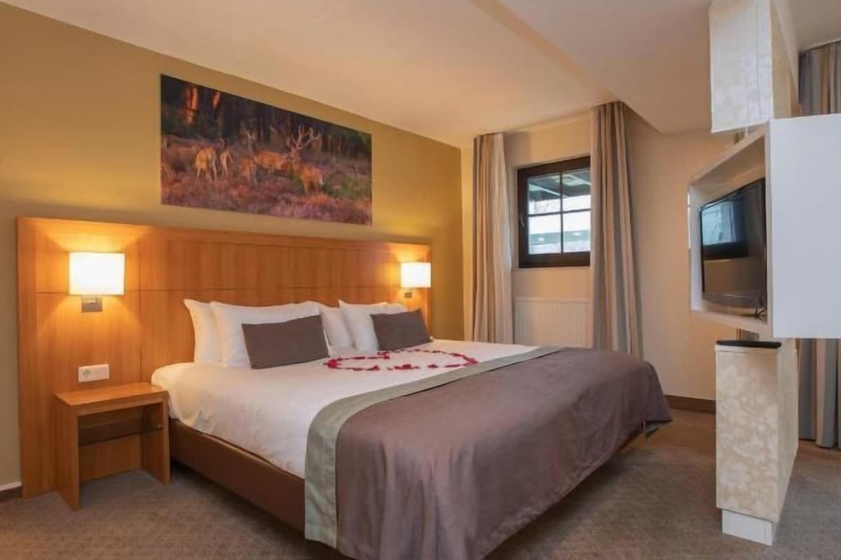 A hotel room with a bed, bedside lamps, a flat-screen TV, and a painting on the wall.