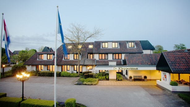 A hotel with a traditional European architectural style, featuring a central entrance with a sign, multiple windows, and a well-maintained garden area. - Fletcher Hotel - Restaurant De Klepperman (Hoevelaken)