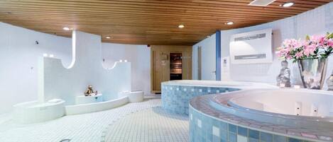 Un spa moderno con varios jacuzzis, techo de madera y suelo de baldosas.