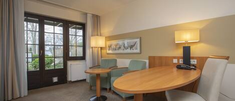 A hotel room with a wooden table, two chairs, a lamp, and a window with curtains.