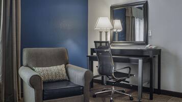 Une chambre d’hôtel avec un fauteuil gris, un bureau avec une lampe et un grand miroir.