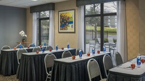 A conference room with tables set for meetings, equipped with water bottles and apples, and large windows offering a view of the outdoors.