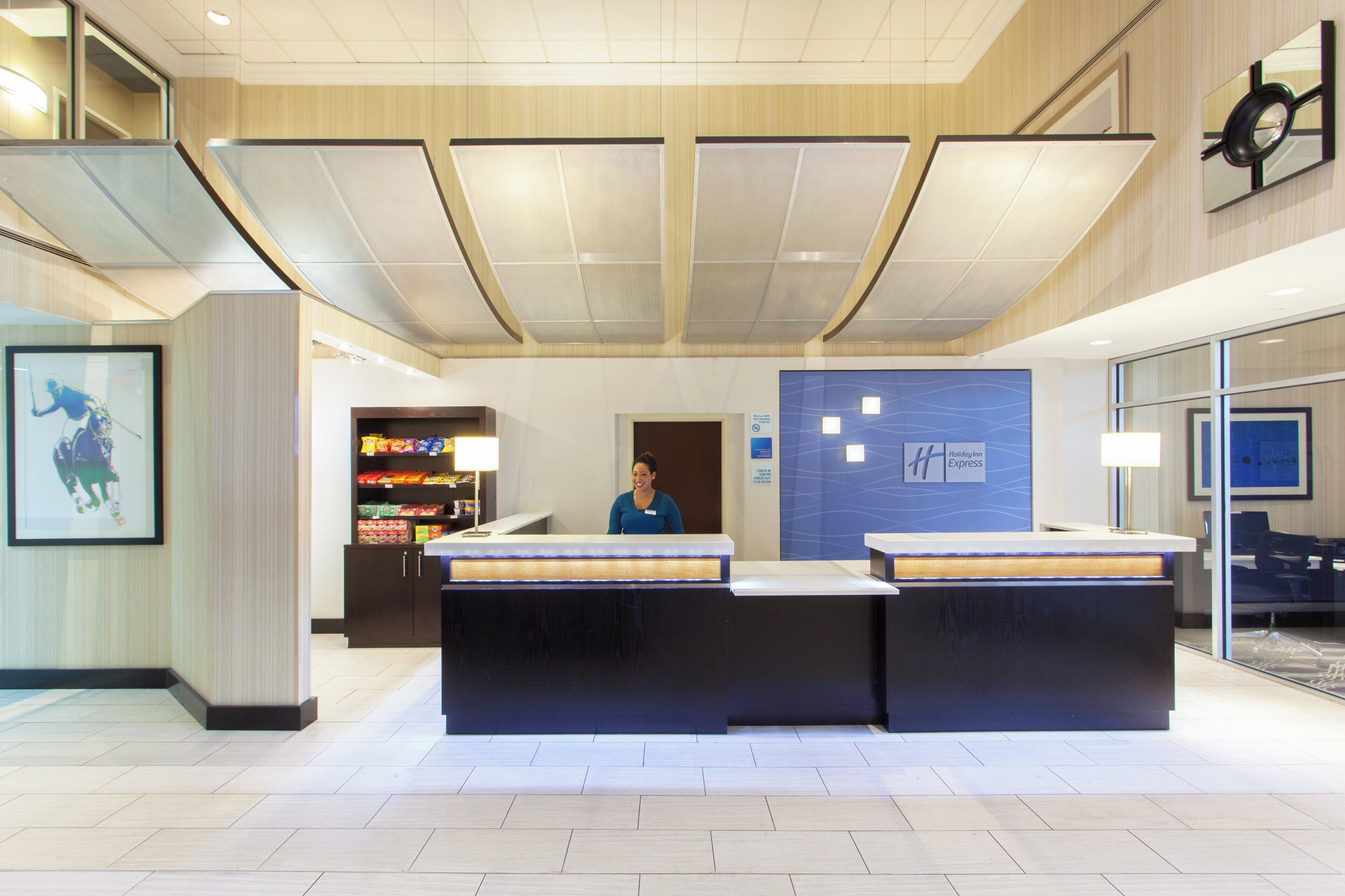 A reception desk with a woman standing behind it, a blue wall with a clock, and a vending machine to the left.