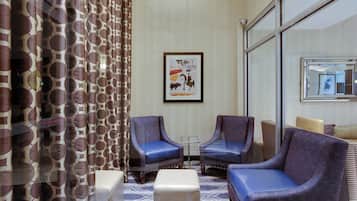 A hotel room with two armchairs, a small table, a sofa, a patterned carpet, and a wall-mounted artwork.