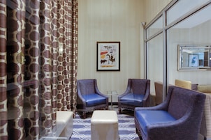 Habitación de hotel con dos sillones, una mesita, un sofá, alfombra estampada y una obra de arte colgada en la pared.