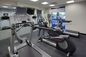 A gym with cardio machines, a mirrored wall, and a view of the outside.