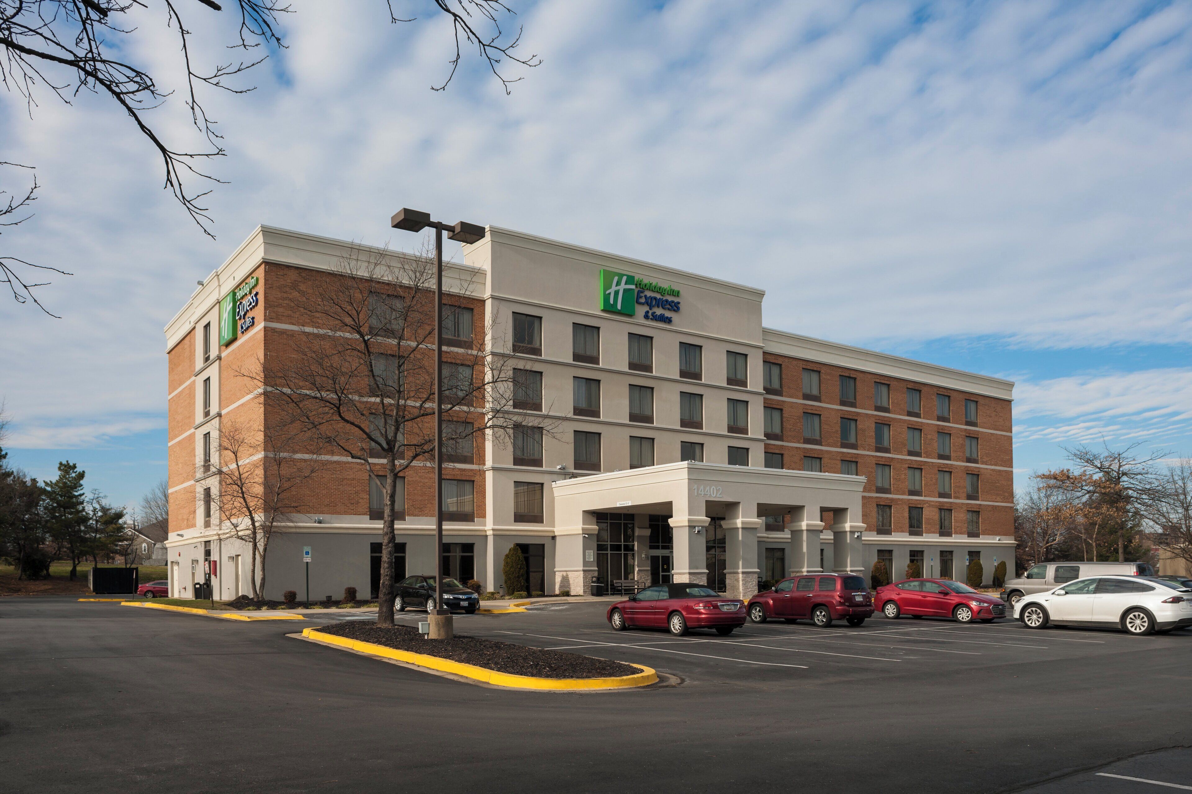 Un hotel Holiday Inn Express con facciata in mattoni, numerose finestre e un parcheggio con diverse auto.