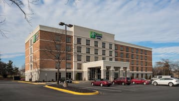 Un hotel Holiday Inn Express con facciata in mattoni, numerose finestre e un parcheggio con diverse auto.