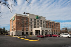 Un hotel Holiday Inn Express con fachada de ladrillo, múltiples ventanas y un estacionamiento con varios coches.
