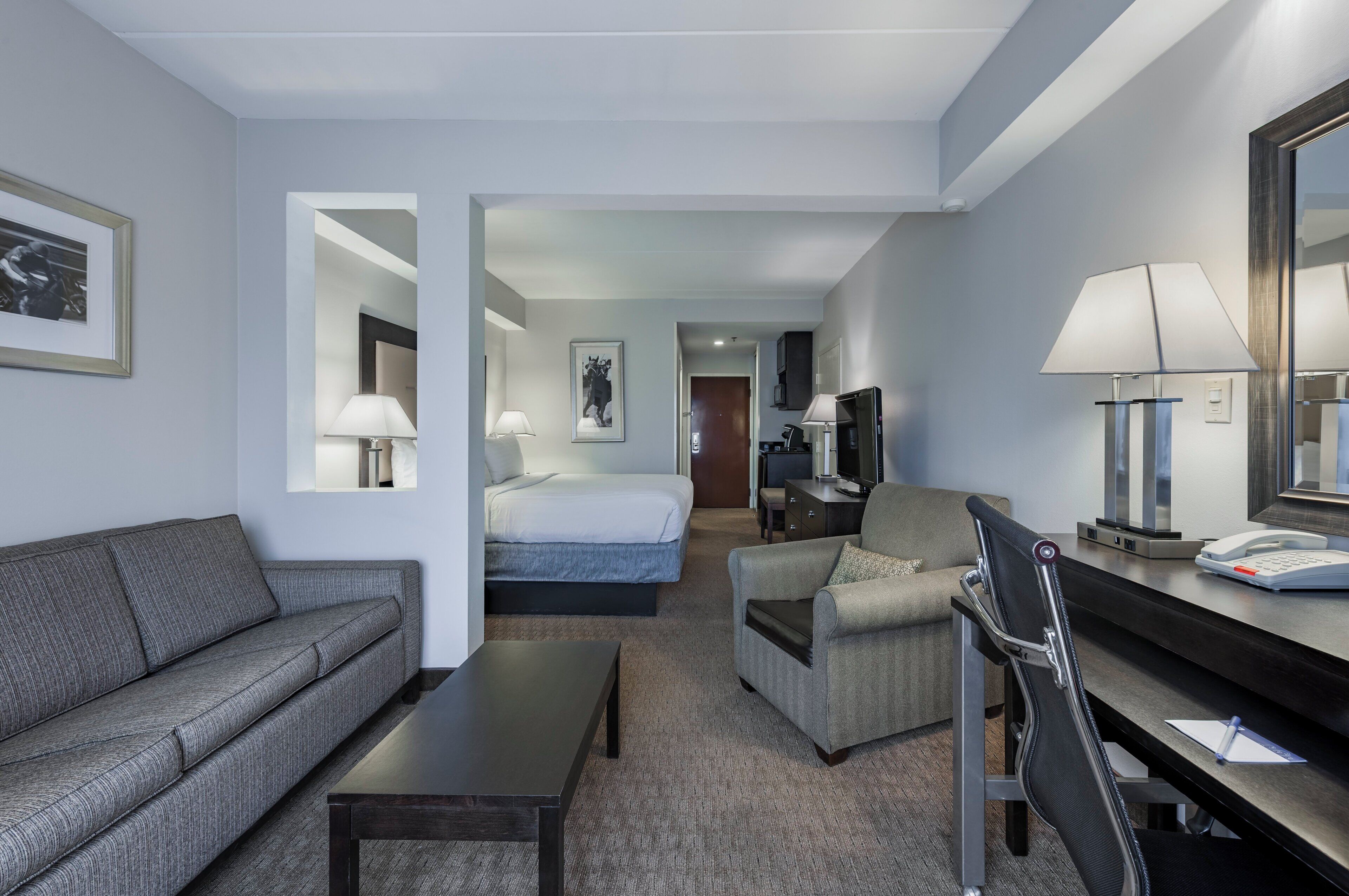 A hotel room with a sofa, a bed, a desk with a lamp, and a chair.
