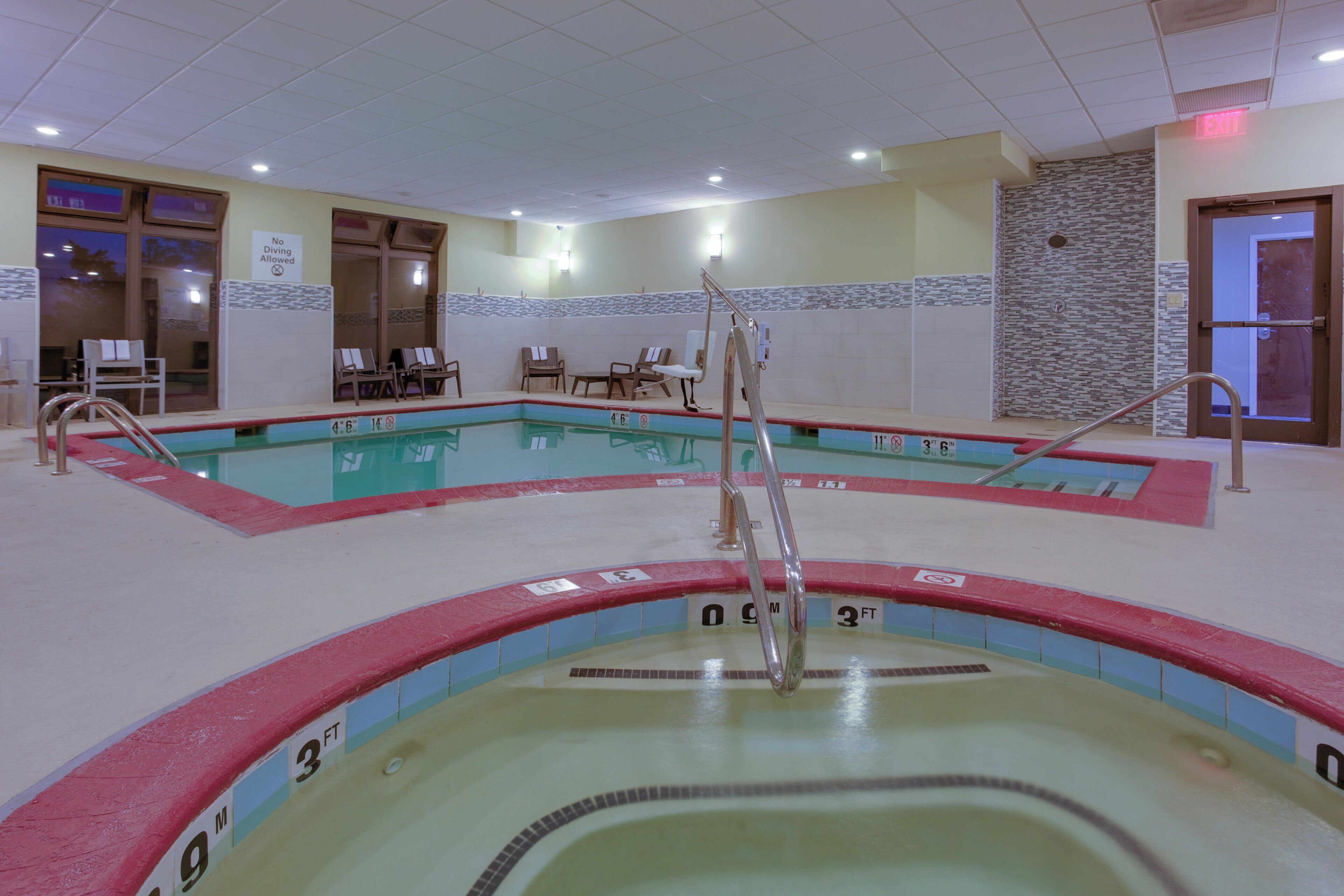 Una piscina interior con múltiples carriles, indicadores de profundidad y sillas de descanso.