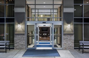 Entrada de un hotel con puerta de cristal, fachada de piedra y un banco afuera.