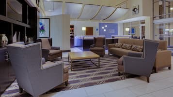 Un hall de hotel con arreglos de asientos, un mostrador de recepción y un amplio ventanal con vistas.