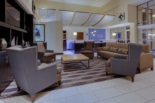 Un hall de hotel con arreglos de asientos, un mostrador de recepción y un amplio ventanal con vistas.