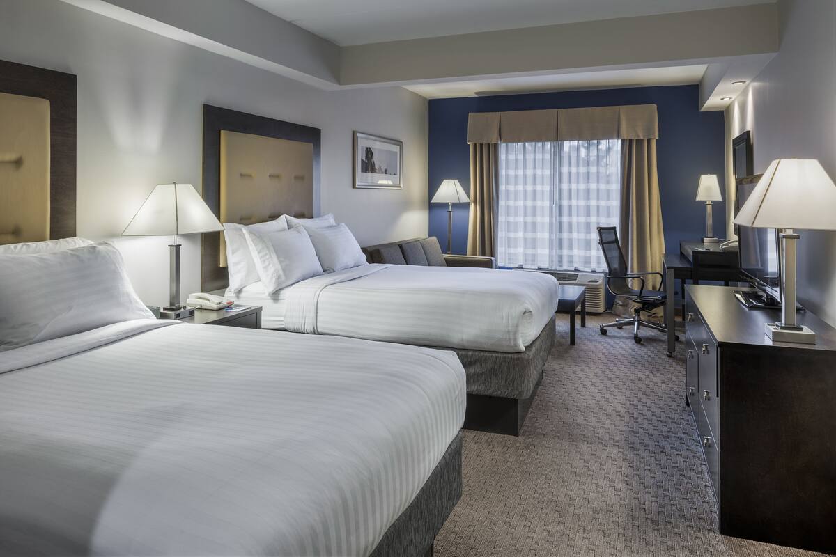 A hotel room with two beds, a desk, a chair, and a television.