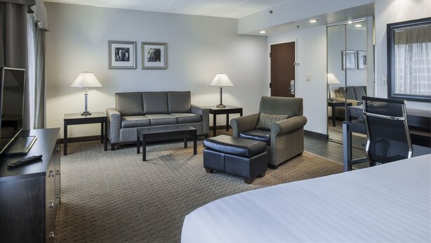 A modern hotel room with a bed, a sofa, a chair, a desk, and a mirror.