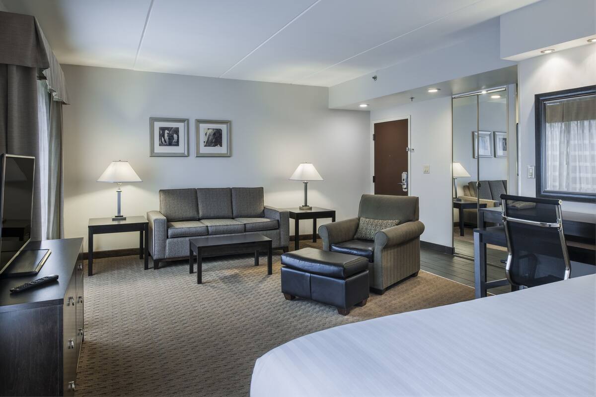 A modern hotel room with a bed, a sofa, a chair, a desk, and a mirror.