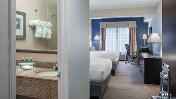 A hotel room with a bathroom, two beds, a desk, and a chair.