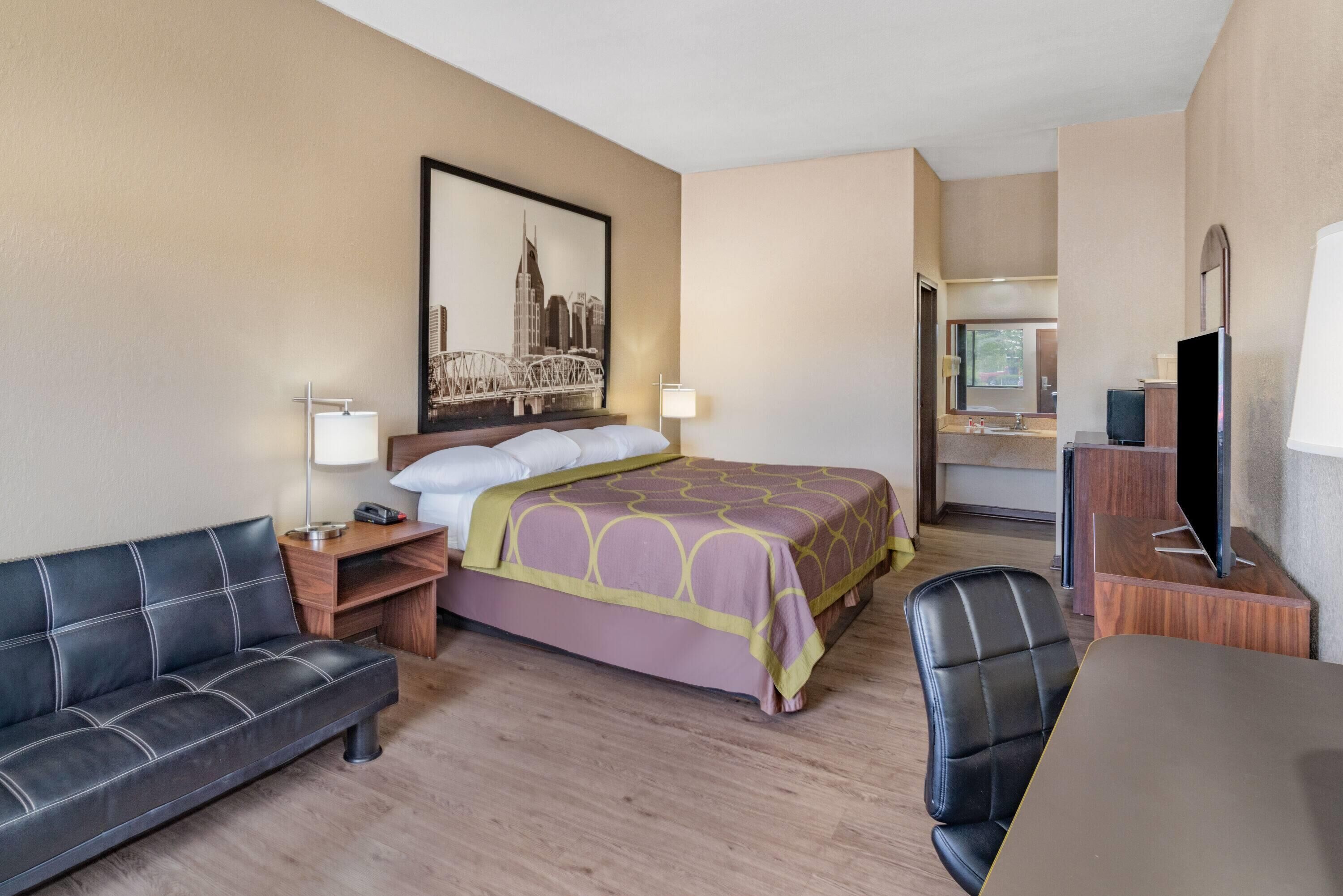 A hotel room with a bed, a desk, a chair, a sofa, and a television.