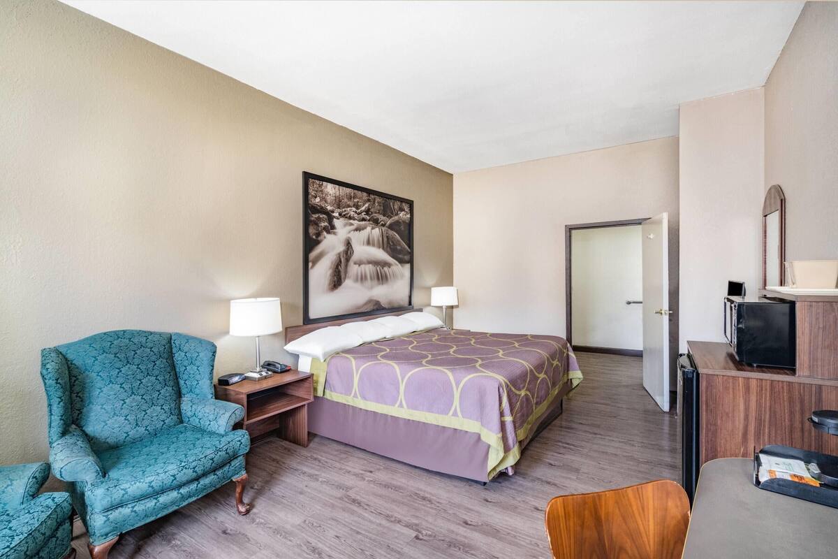 A hotel room with a bed, a chair, a desk, a lamp, and a television.