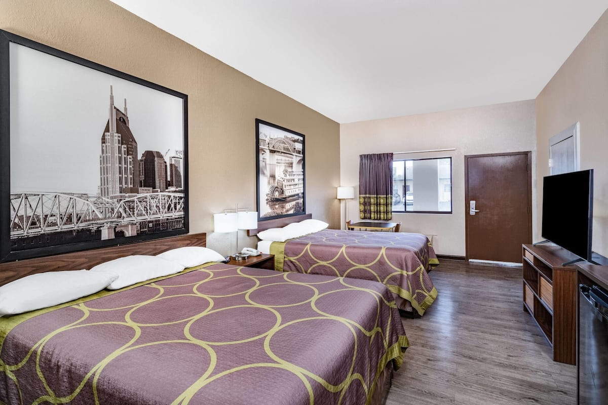 A hotel room with two beds, a TV, a desk, and a window with curtains.