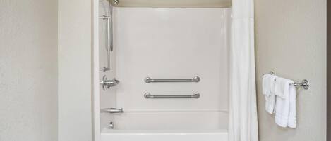 A standard hotel bathroom with a bathtub, shower, and handrails.
