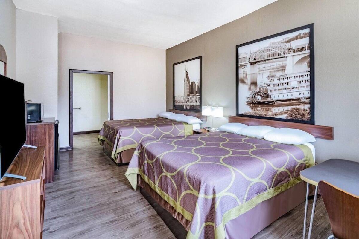 A hotel room with two beds, a desk, a TV, and large framed pictures on the wall.
