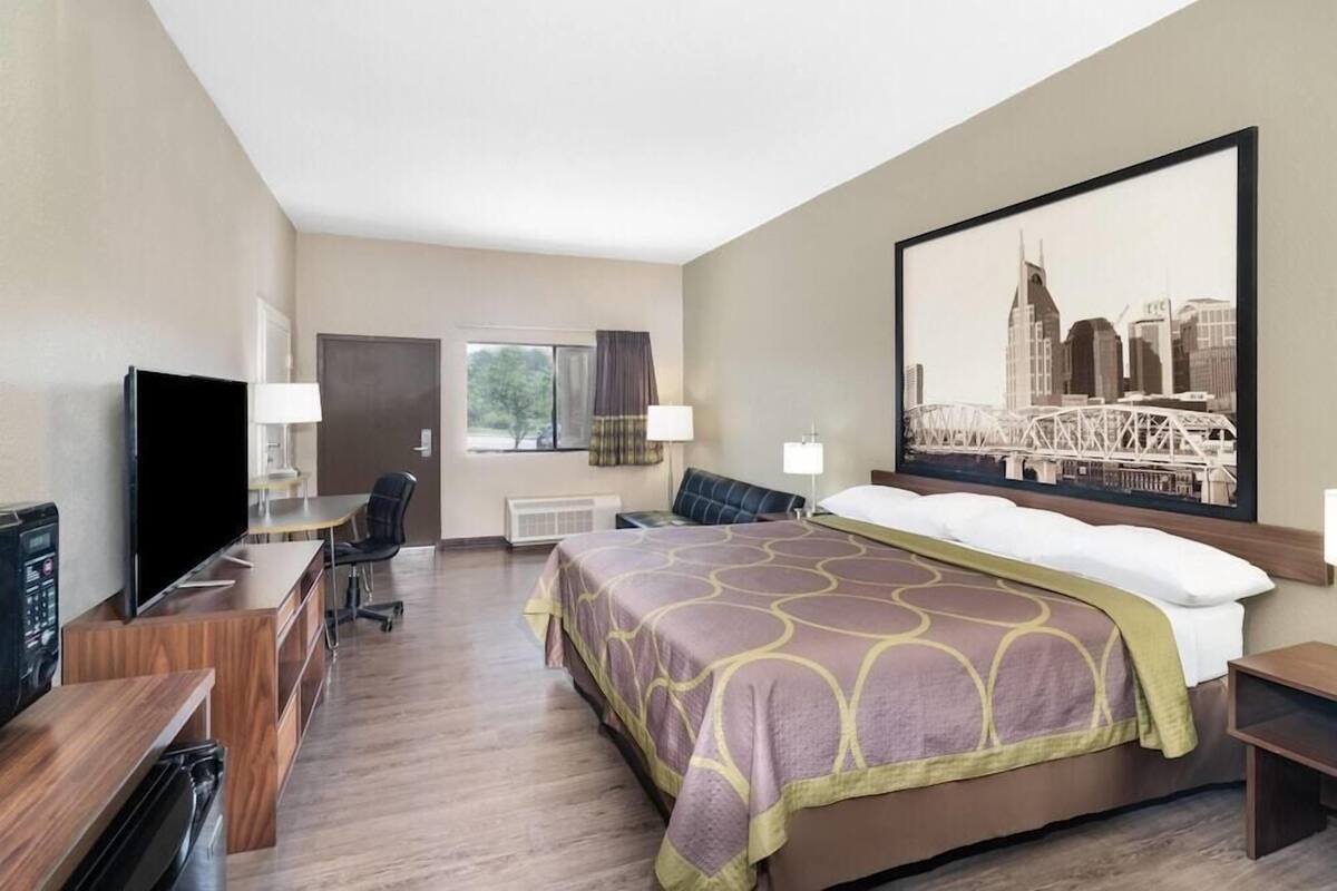 A hotel room with a bed, a desk, a television, and a large window.