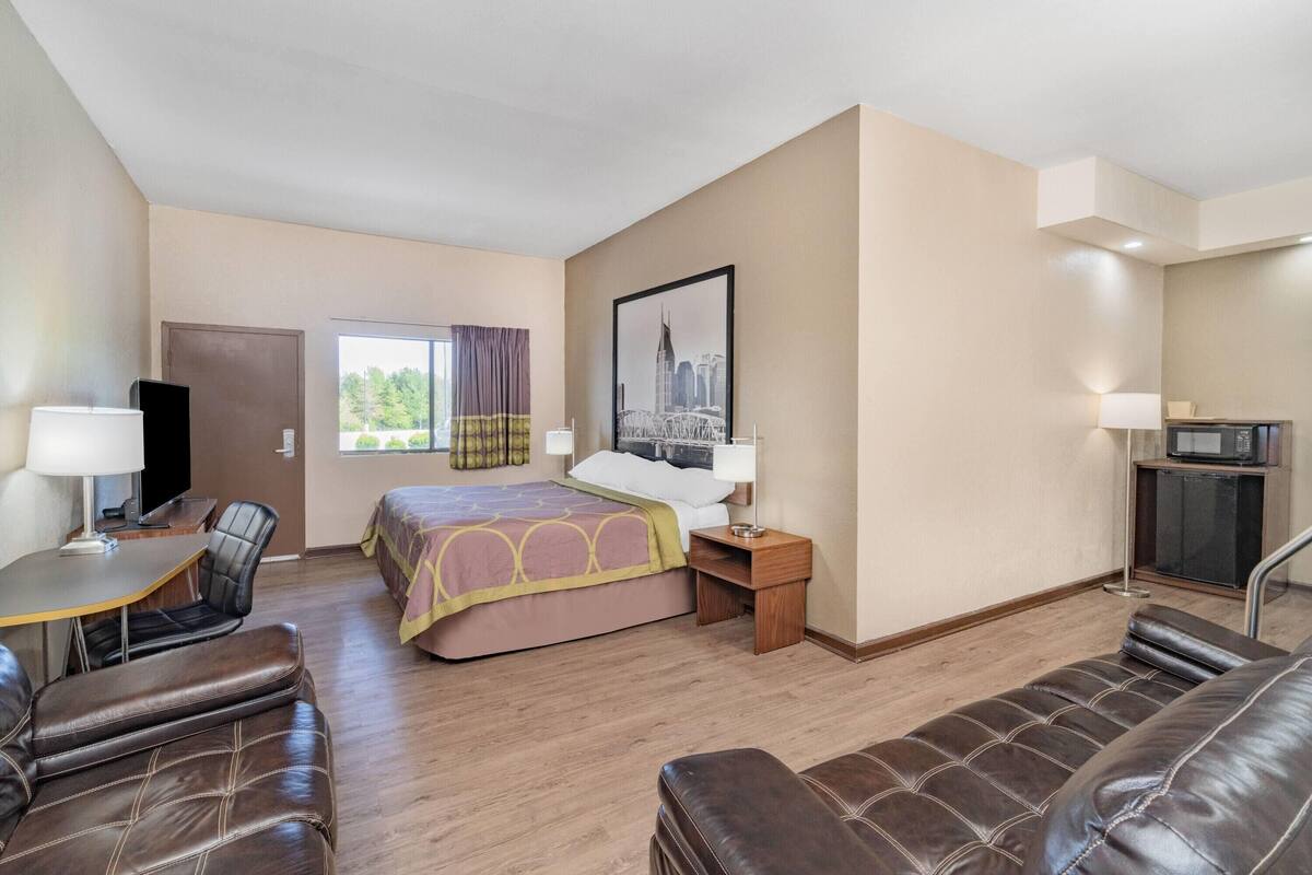 A hotel room with a bed, a desk, a chair, a sofa, a TV, and a window with curtains.