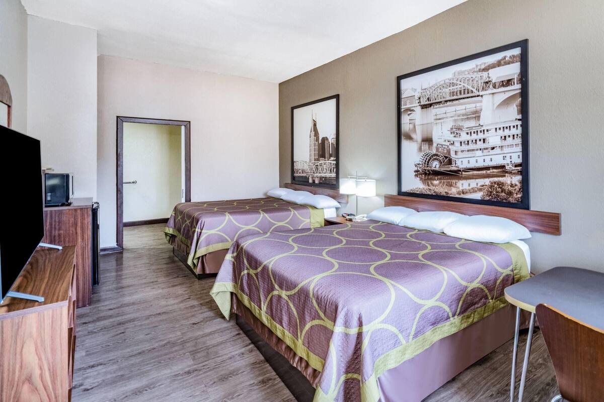 A hotel room with two beds, a desk, a TV, and two large framed pictures on the wall.