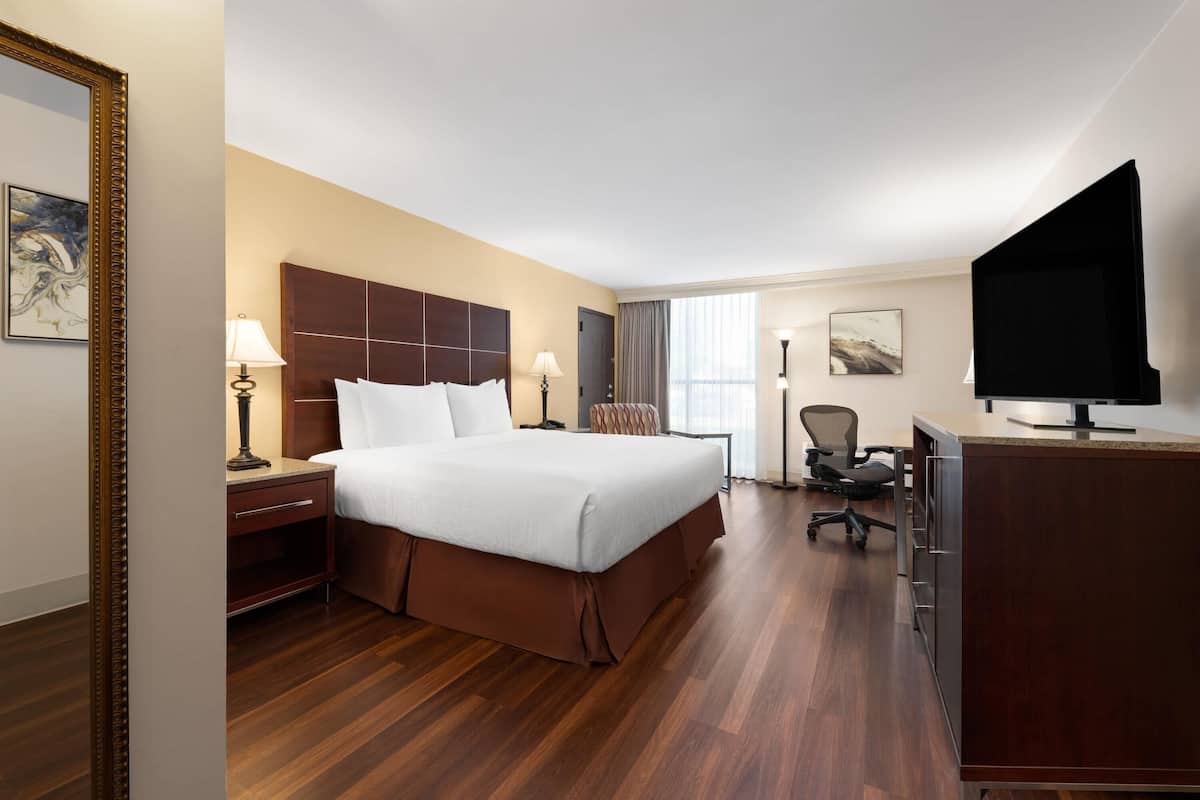 A hotel room with a large bed, a desk, a chair, a TV, and a window with curtains.