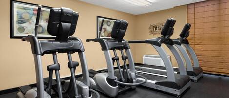 Tres máquinas elípticas en un gimnasio con paredes color crema y un cuadro en la pared.